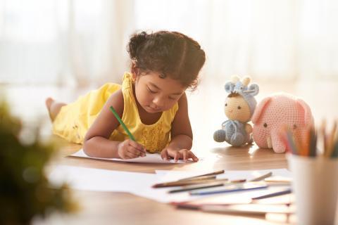 Young child lying on the floor coloring pages with crayons