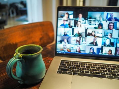 Laptop computer monitor with screen open on a wooden tabletop alongside a ceramic cup.